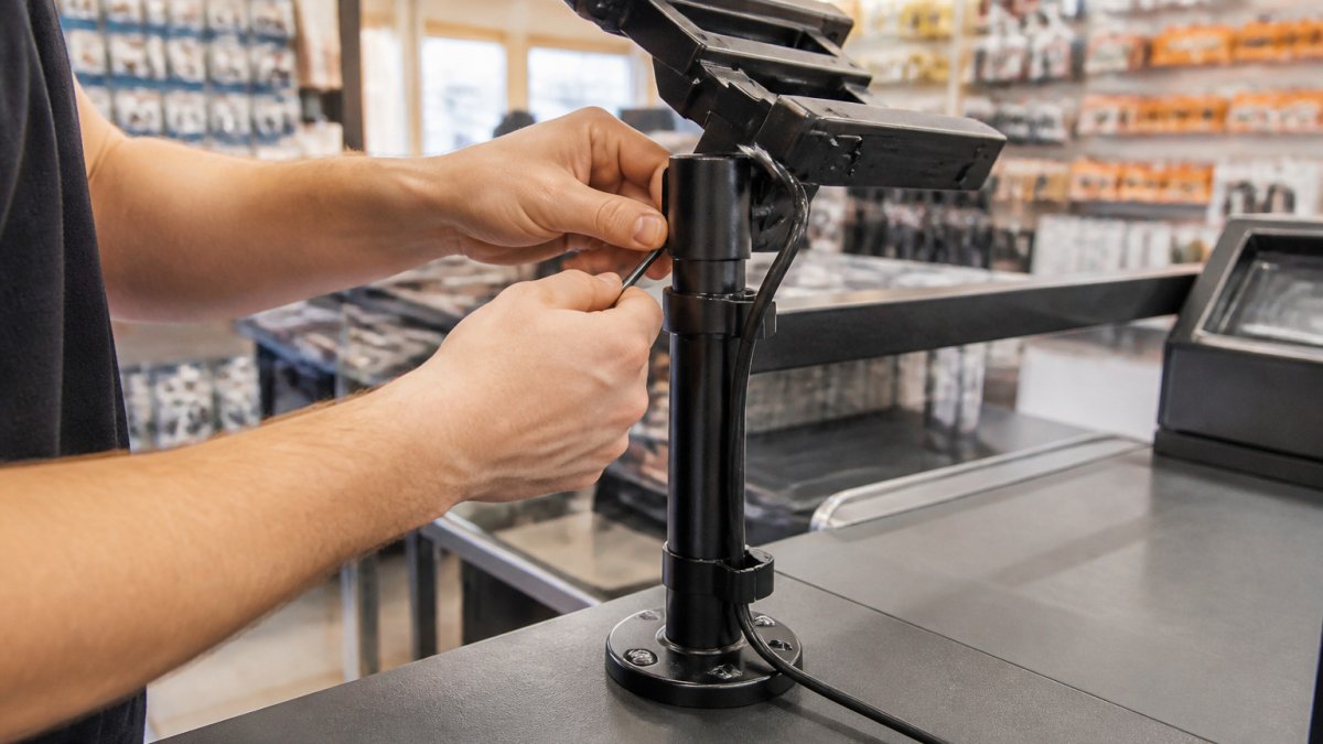 Mitarbeiter bei der modularen POS Montage einer Terminal-Halterung mit sauberem Kabelmanagement am Kassentresen